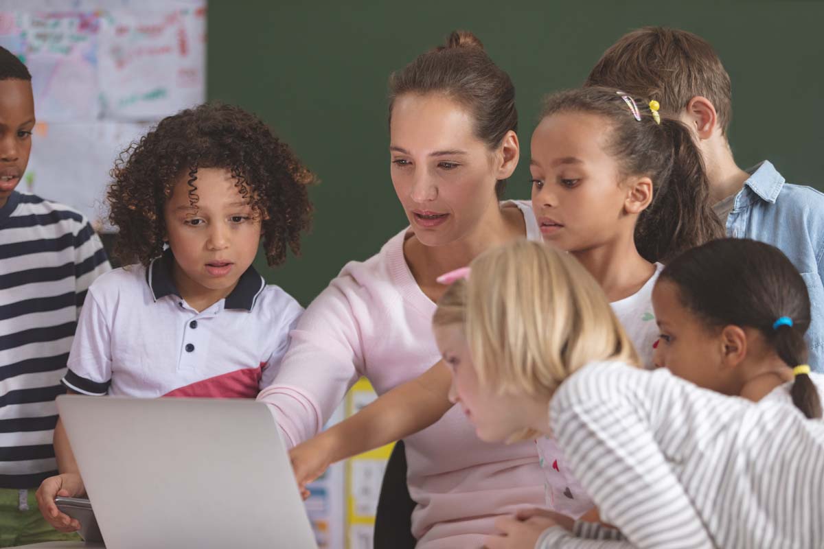 Group of children crowded around teacher and her laptop
